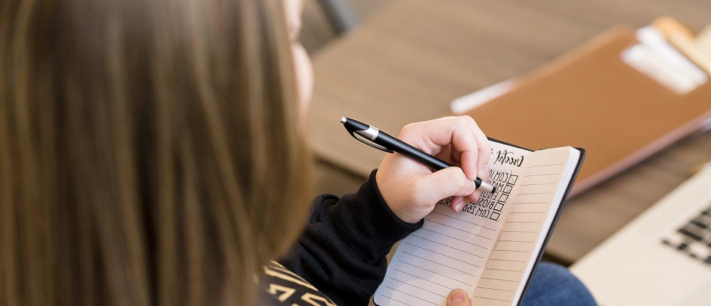 An 韦德体育app官网 student making check marks next to courses listed in a notebook.